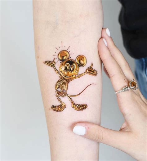 Gold Mickey Mouse Tattoo Located On The Inner Forearm